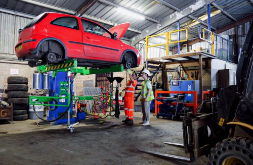 Red scrap car being inspected by workers at a scrap yard