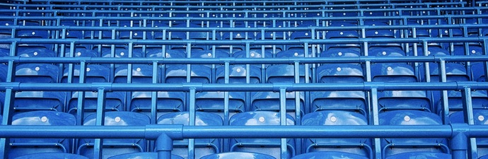 Multiple rows of empty blue chairs at the Chelsea Football Club stadium.