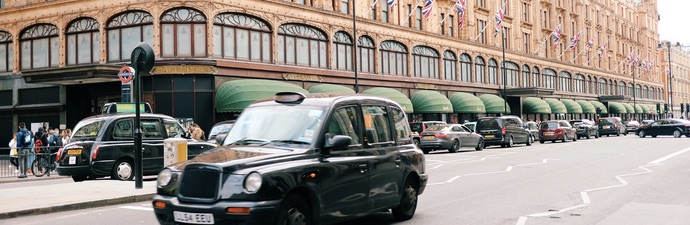 Exterior of the Harrods department store in London with black cab driving past.