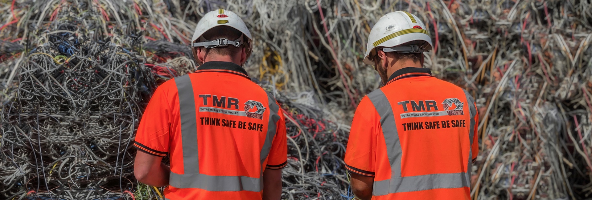 Two scrap metal workers both wearing orange TMR branded hi vis t-shirts and hard hats, sorting scrap wire.
