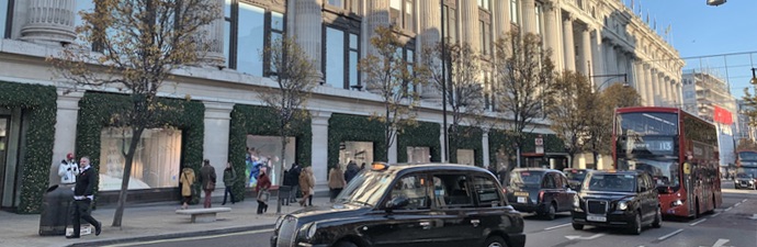 Exterior of the Selfridges department store on Oxford Street with black cabs and a red bus driving past.