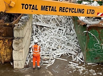 TMR worker wearing orange hi vis, standing infront of a pile of upvc window frames.