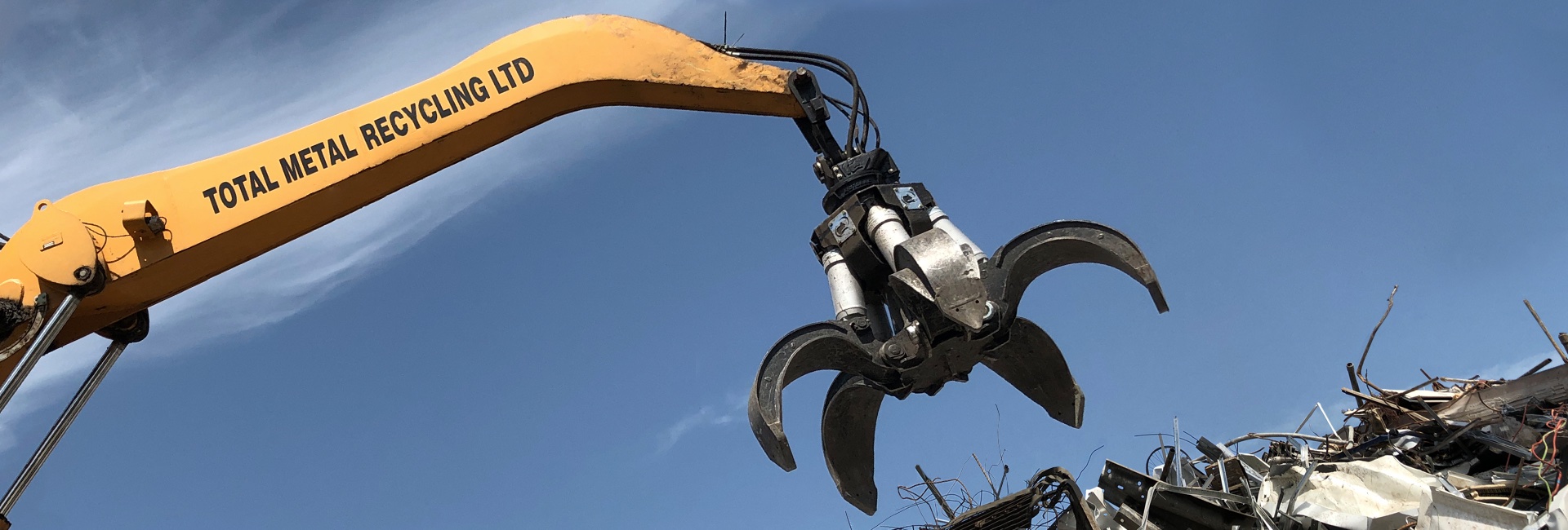 Yellow TMR branded scrap metal grabber against a blue sky.